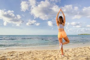 Back young woman on one leg yoga position at the beach